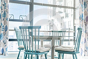 Very bright dining area in an apartment, with large windows in the background, and blue chairs with a glass table in the