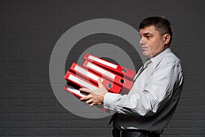 Very busy businessman closeup portrait, posing with red folders, overworking concept, dark wall background