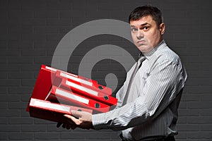 Very busy businessman closeup portrait, posing with red folders, overworking concept, dark wall background