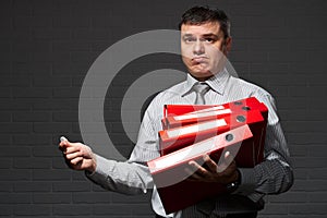 Very busy businessman closeup portrait, posing with red folders, overworking concept, dark wall background