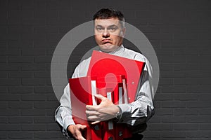 Very busy businessman closeup portrait, posing with red folders, overworking concept, dark wall background