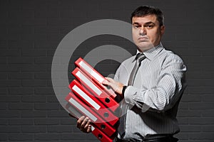 Very busy businessman closeup portrait, posing with red folders, overworking concept, dark wall background