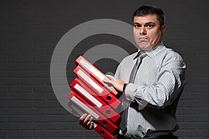 Very busy businessman closeup portrait, posing with red folders, overworking concept, dark wall background