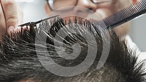 A very close-up of men`s hands with a hairdresser in glasses cutting hair with scissors.