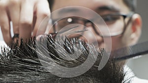 A very close-up of men`s hands with a hairdresser in glasses cutting hair with scissors.