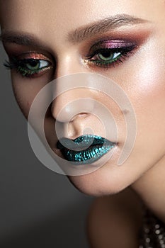 A very close up portrait of a beautiful young girl with bright colorful trendy smoky eyes and blue sparkle lips.