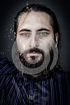 Very close-up portrait of a young bearded man with an intense gaze with streams of water running down his face