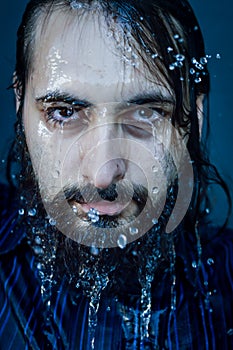 Very close-up portrait of a young bearded man with soggy face and intense gaze with streams of water running down his face