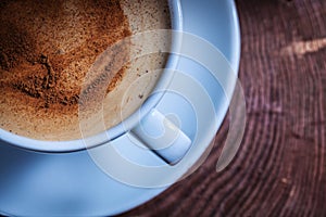 Very close up view from above coffee with foam and cinnamon in white ceramic cup on vintage cross section tree trunk