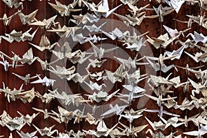 Very close view of 1000 origami folded paper cranes sculpture against a background of old red tin siding