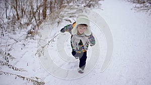 A very cute happy little boy runs in the Park in winter. Winter time. Happy boy having fun in a snow winter park. He is