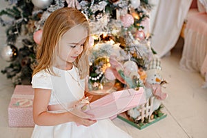 Very cute little girl blonde in a white dress holding a gift box