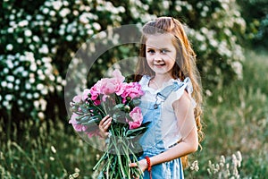 Very cute little girl with flowers in a denim sundress  posing at the sunset