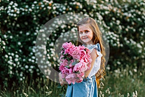 Very cute little girl with flowers in a denim sundress  posing at the sunset