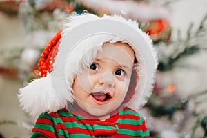 Very cute portrait of little baby boy in Santa hat on Christmas tree lights background bokeh. new year, family, son