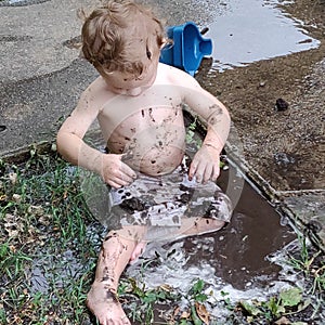 A very dirty child playing in a mud puddle