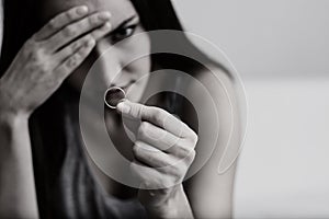 Very disappointed and offended wife depressed after divorce, holding with hand a wedding ring sitting on a room floor. Black and w