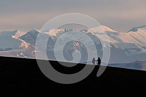 A very distant couple shaking hands on top of a mountain with distant hills and mountains covered by snow