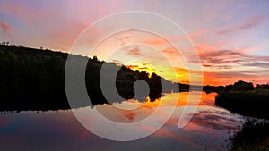 Very dramatic sunset scene. Colours red, orange, violet and reflections in the water. Horizontal panoramic view of a sunset