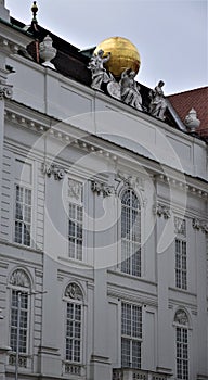 Very elegant and stately facade of a white building in Vienna. On the cornice two, of the three statues, support a large golden sp