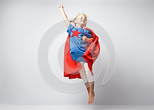 Very excited little girl dressed like superhero jumping alongside the white wall.