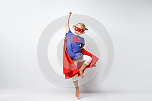 Very excited little girl dressed like superhero jumping alongside the white wall.