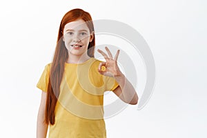 Very good. Cute little girl with long ginger hair and freckles shows okay sign, smile and say yes, praise something