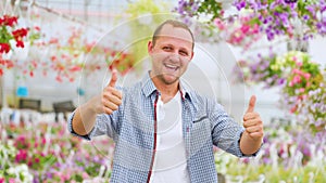 A very happy lucky man stands in a greenhouse and shows thump up with both hands.