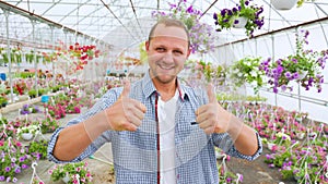 A very happy lucky man stands in a greenhouse and shows thump up with both hands