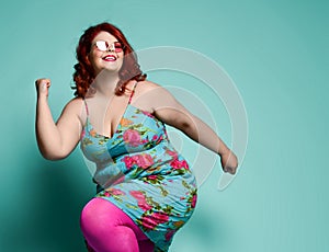 Very happy lucky plus-size lady overweight woman in fashion sunglasses and colorful sundress dancing, celebrating