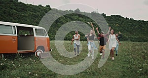 Very happy running and jumping group of friends , in the middle of field, beside orange vintage van