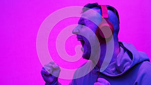 Very happy Young man in headphones on a pink background, a man listens to music in overhead headphones