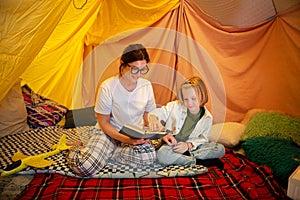 A very kind and warm looking mother is laying on her stomach next to her son reading him a book aloud and teaching him photo