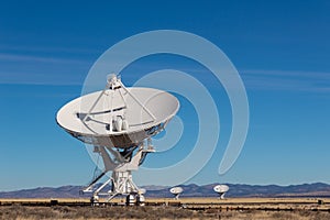 Very Large Array radio antenna dish close with others in distance, blue sky photo