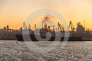 A very large container ship sailed to load containers at the industrial sea port. The ship is transport. Cranes load cargo