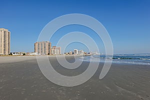 Very large wet sandy beach by the ocean with high rise condominium buildings in the background