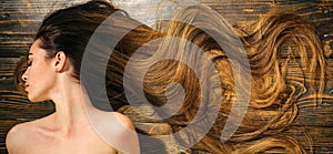 Very long hair on wooden background. Beautiful model with curly hairstyle. Hair Salon concept. Care and hair products.