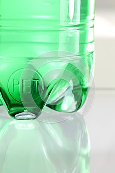 Very nice detail of green plastic sparkling water bottle placed on glass with beautiful reflections of light for an elegant and ab