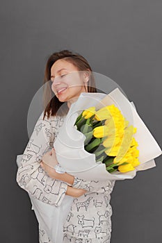 Very nice young happy woman holding big and beautiful blossoming bouquet of fresh yellow tulips flowers on the grey wall