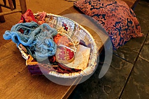 Very old antique sewing or haberdashery basket with wool, yarn, thread and various pieces of linen and other textiles, on an old w