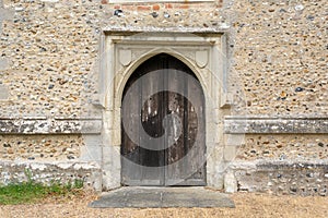 Very old arched wooden church door with stone wall. Hertfordshire. UK