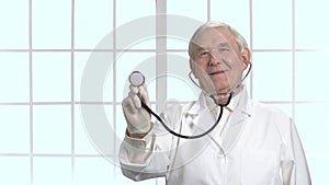 Very old doctor using stethoscope in hospital.