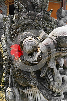 Very old dragon head shape stone sculpture covered with moss and lichens in Bali and decorated with red flower blossom