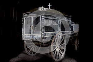 Very old and dusty hearse made of wood with large wooden wheels. Used to transport the coffin with the dead during the funeral in