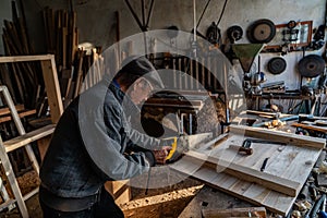 Very old master carpenter in glasses and grey clothes working hard in his home workshop, sawing board
