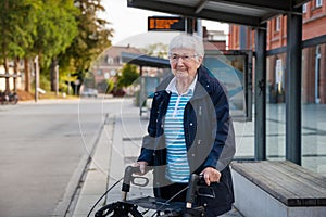 Very old senior woman waiting at the bus stop with walker