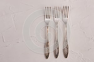 Very old set of three rusty vintage silver forks on a white cement texture background