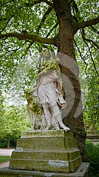 A very old statue covered with green moss. Woman with a hunting dog