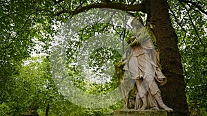 A very old statue covered with green moss. Woman with a hunting dog