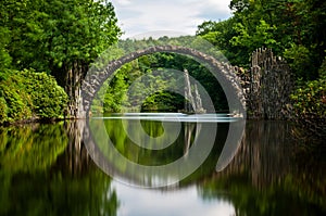 Very old stone bridge over the quiet lake with its reflection in the water